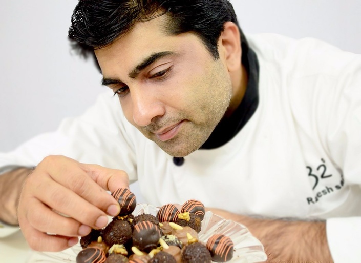A pastry chef carefully arranges chocolate truffles on a plate, showcasing attention to detail.